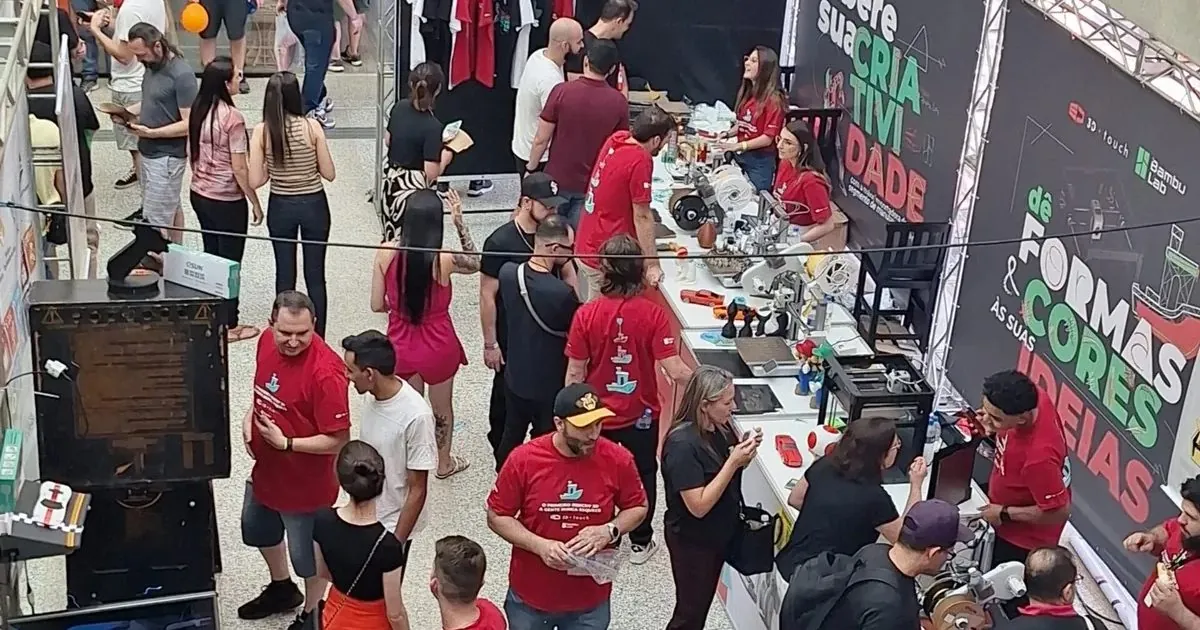 Multidão de visitantes entre estandes de impressão 3D em pavilhão de feira