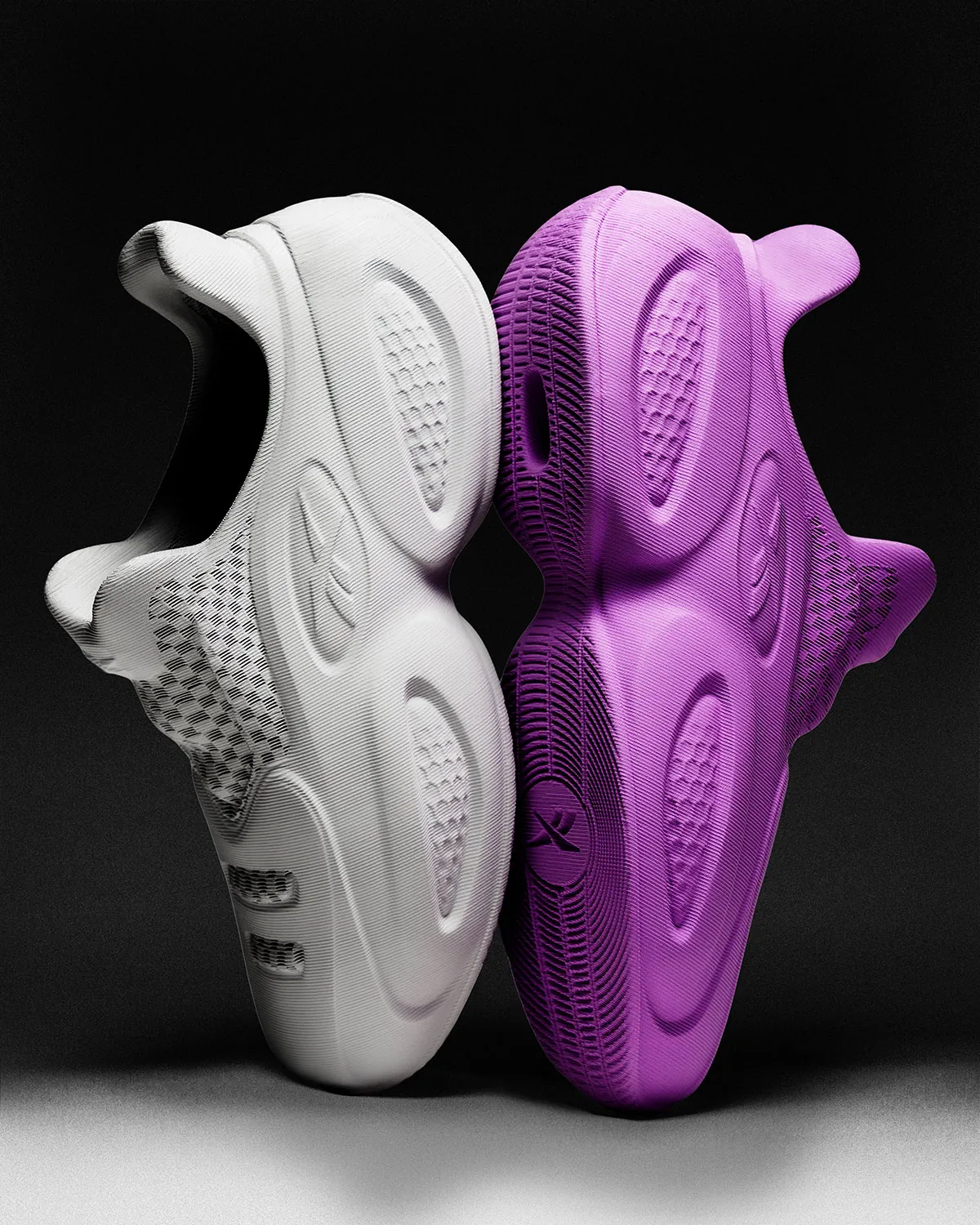Os dois colorways do Reebok Question 96/26 impresso em 3D, Stone e Lilac, apoiados sola contra sola em fundo escuro